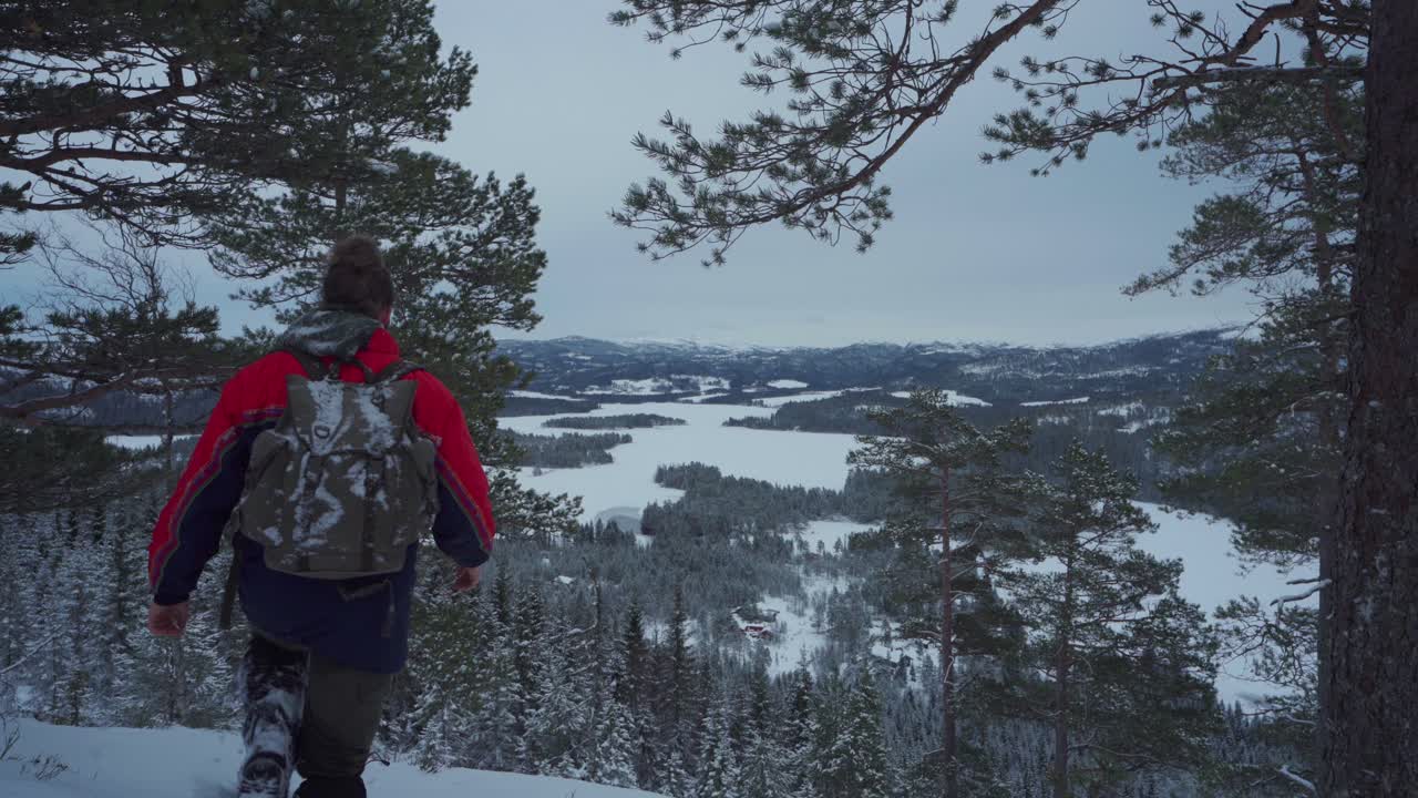 caminante con mochila admira la belleza del bosque cubierto de nieve en invierno desde la montaña