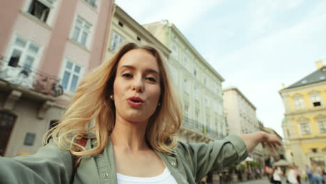 close-up view of caucasian blonde young woman speaking and waving to the camera in the street while holding it