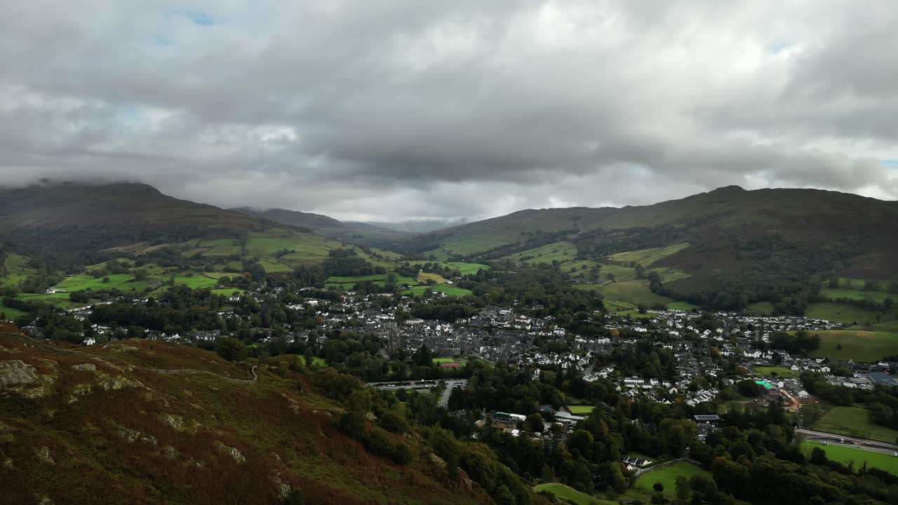 Aerial drone shot flying over hills in the Lake District to reveal the town of Ambleside. Ambleside, Lake District, UK