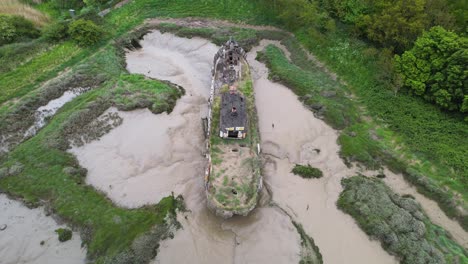 Vista-Aérea-De-Un-Barco-Más-Ligero-Atascado-En-El-Barro-En-El-Parque-De-Campo-Wat-Tyler,-Basildon-Nublado,-Reino-Unido---Inclinación,-Disparo-De-Drones