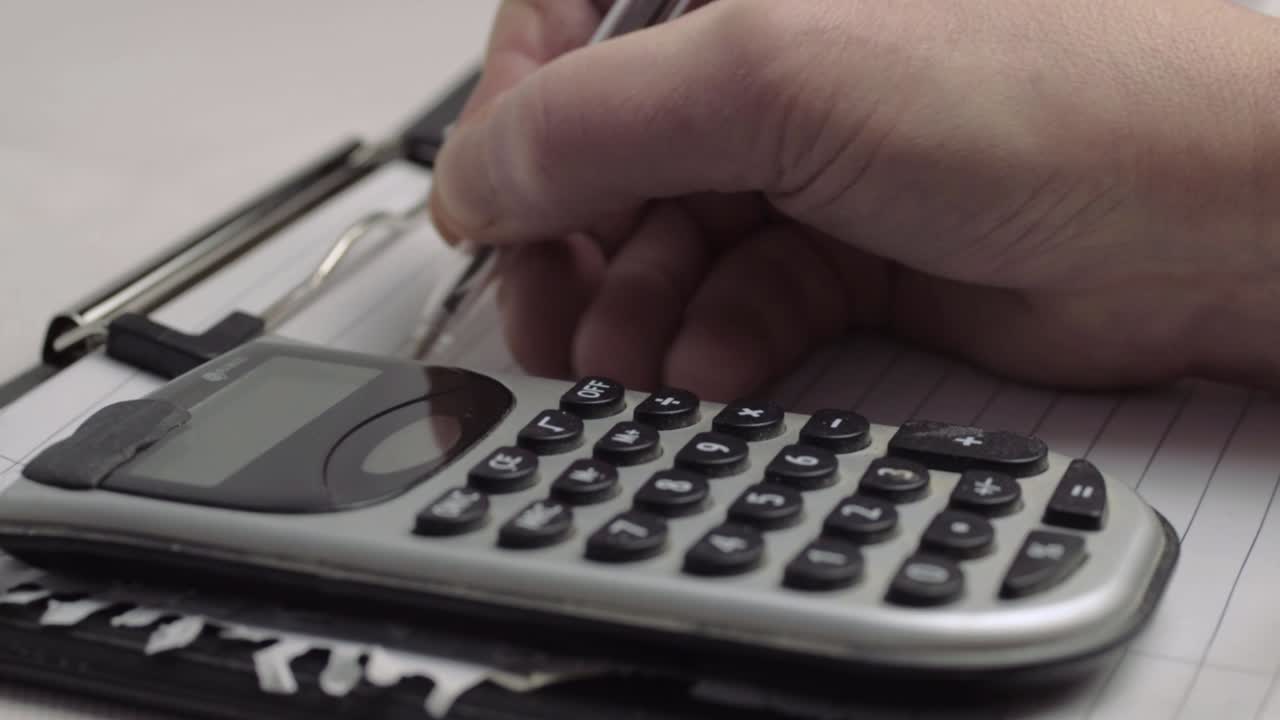 Hand writing financial information on clipboard with calculator