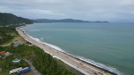 Vista-Aérea-De-Una-Impresionante-Carretera-Costera-Que-Serpentea-A-Lo-Largo-De-Una-Vasta-Bahía-Oceánica-En-Una-Exuberante-Isla-Tropical,-Que-Muestra-Una-Vegetación-Vibrante-Y-Aguas-Cristalinas.