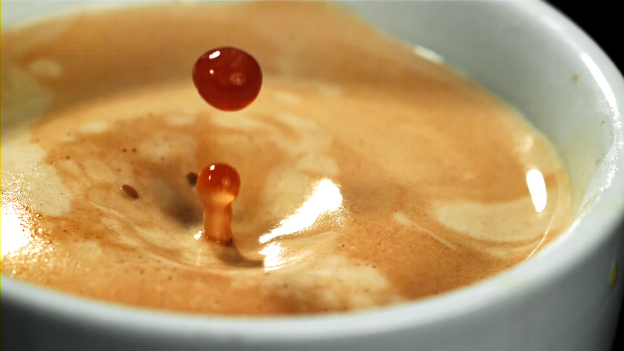 Goccia di caffè al rallentatore che schizza nell'espresso con crema