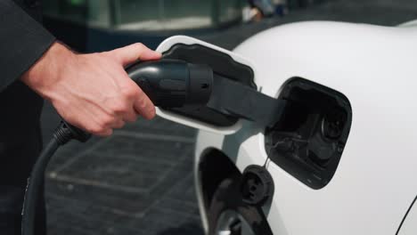 un hombre de negocios progresista desconecta el enchufe del cargador del punto de carga de su coche ev.