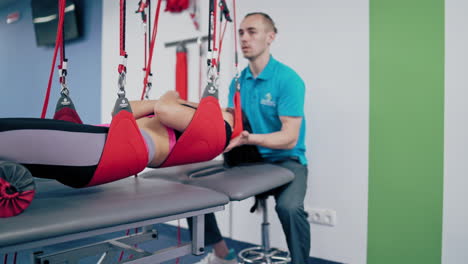 woman is hanging on special suspension ropes in rehabilitation center. modern equipment for undergoing physiotherapy for a young female.personal trainer and a patient in modern center.