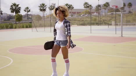 young woman with skateboard poses by ball court