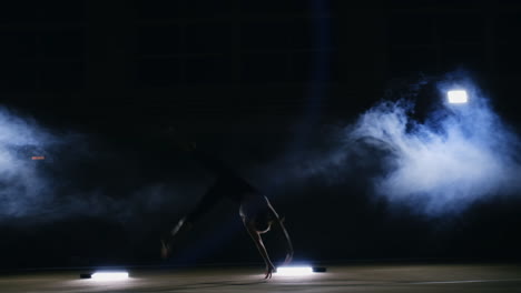 talented girl gymnast performs a flip turn in a jump on the gymnastics carpet in slow motion in a contoured light in the smoke. steadycam. the rotation in the air. acrobatics