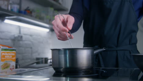 cook stirs boiling sauce by spiral whisk in stewpan