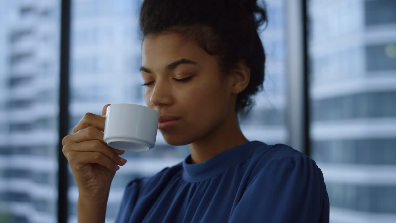 Businesswoman drinking coffee in modern office. Female manager looking in window
