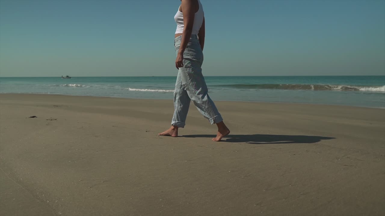 청록색 물과 함께 해변의 해안을 따라 천천히 걷는 젊은 갈색 머리 소녀