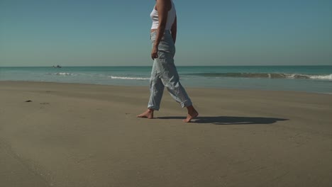joven morena caminando lentamente a lo largo de la orilla de una playa, horizonte de fondo con agua turquesa