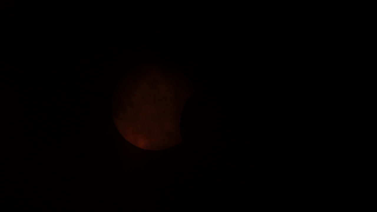 Partial solar eclipse being covered by clouds, reemerging, and then being covered again