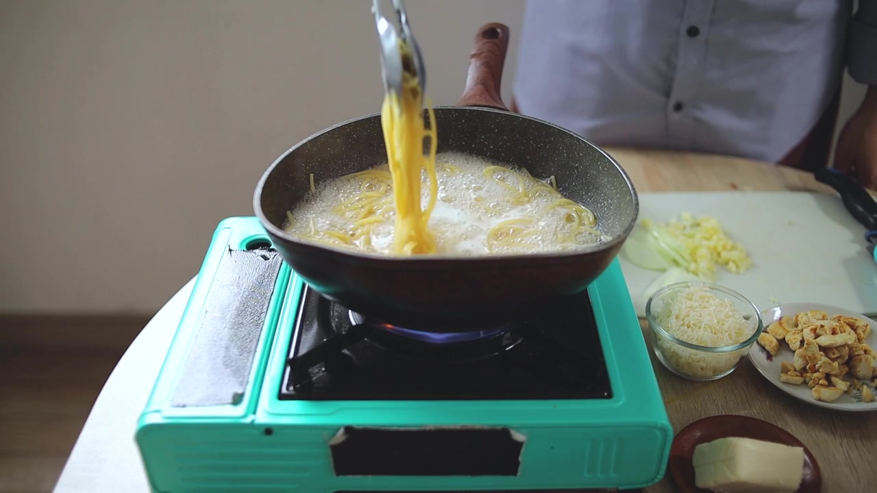 Home cook stirring and checking spaghetti boiling in bubbling hot water with kitchen tongs