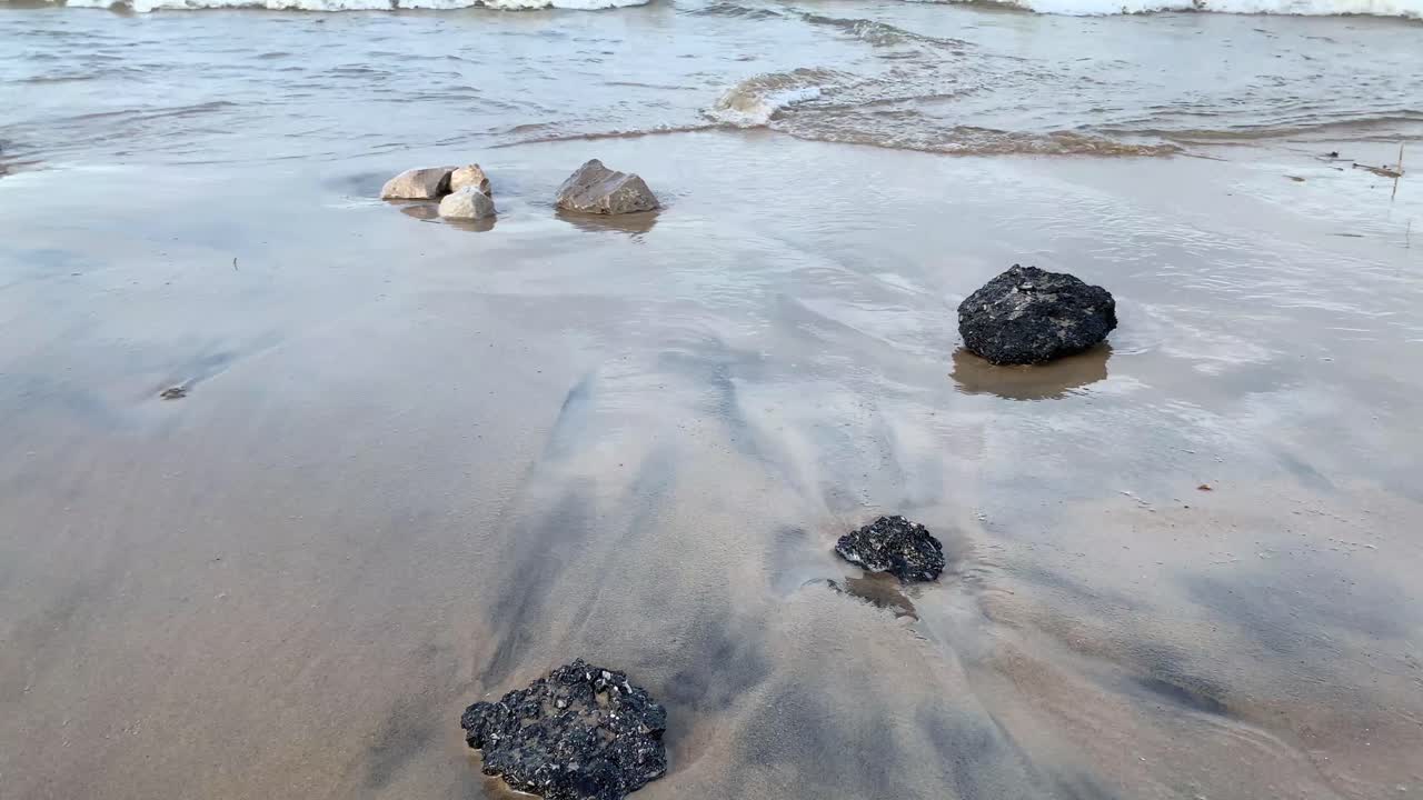 rocce nere di asfalto sulla spiaggia nella sabbia bagnata