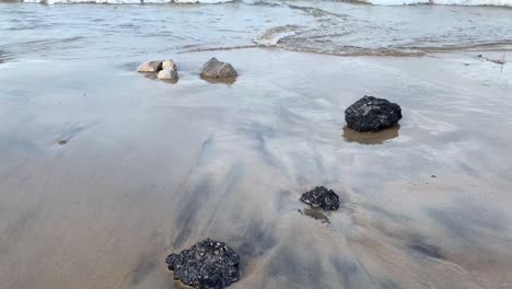 Rocas-De-Asfalto-Negro-En-La-Playa-En-La-Arena-Mojada