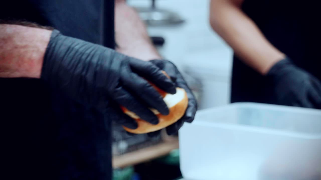 4K Cinematic food cooking footage of a chef preparing and making a delicious homemade burger in a restaurant kitchen in slow motion