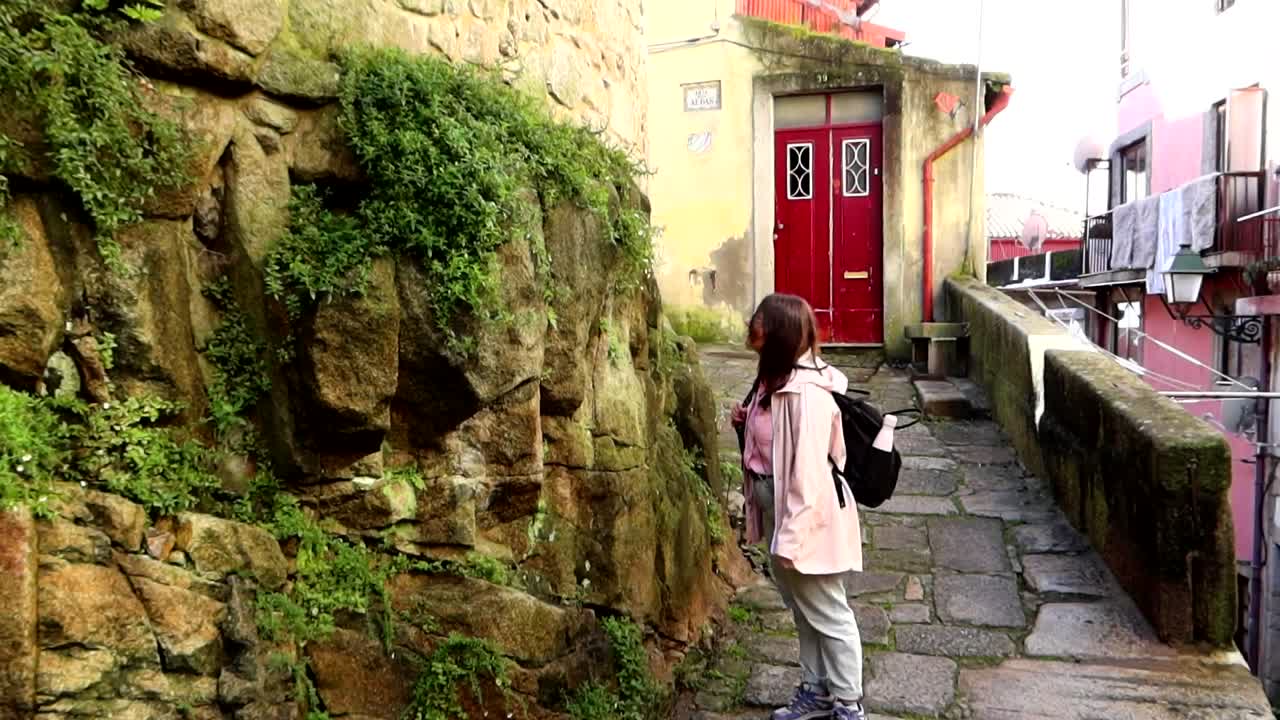 mujer admirando las plantas que crecen en una pared de roca al final de la estrecha calle rua das aldas en oporto, portugal