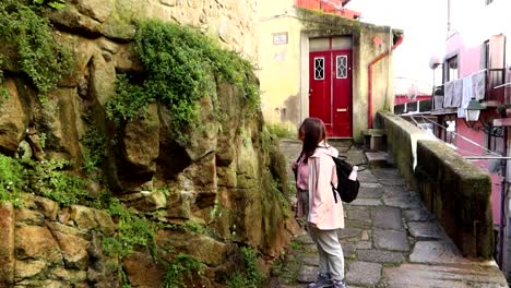 Woman-admiring-the-plants-that-grows-on-a-rock-wall-at-the-end-of-the-narrow-Rua-das-Aldas-street-in-Porto,-Portugal