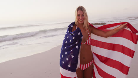 Caucasian-woman-holding-and-waving-an-US-flag-on-the-beach.