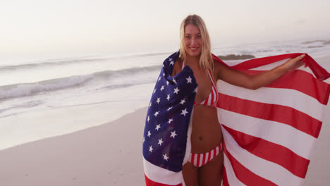 caucasian woman holding and waving an us flag on the beach.