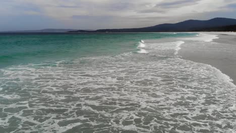 Aerial-view-low-over-waves-at-a-beach,-in-cloudy-New-south-wales,-Australia