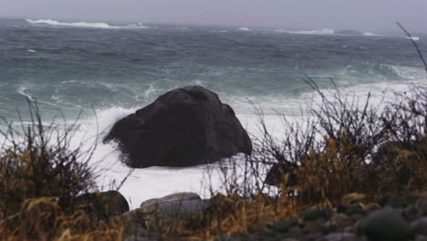 waves crashing on a rock by the coast of arendal in norway on a stormy day - wide shot