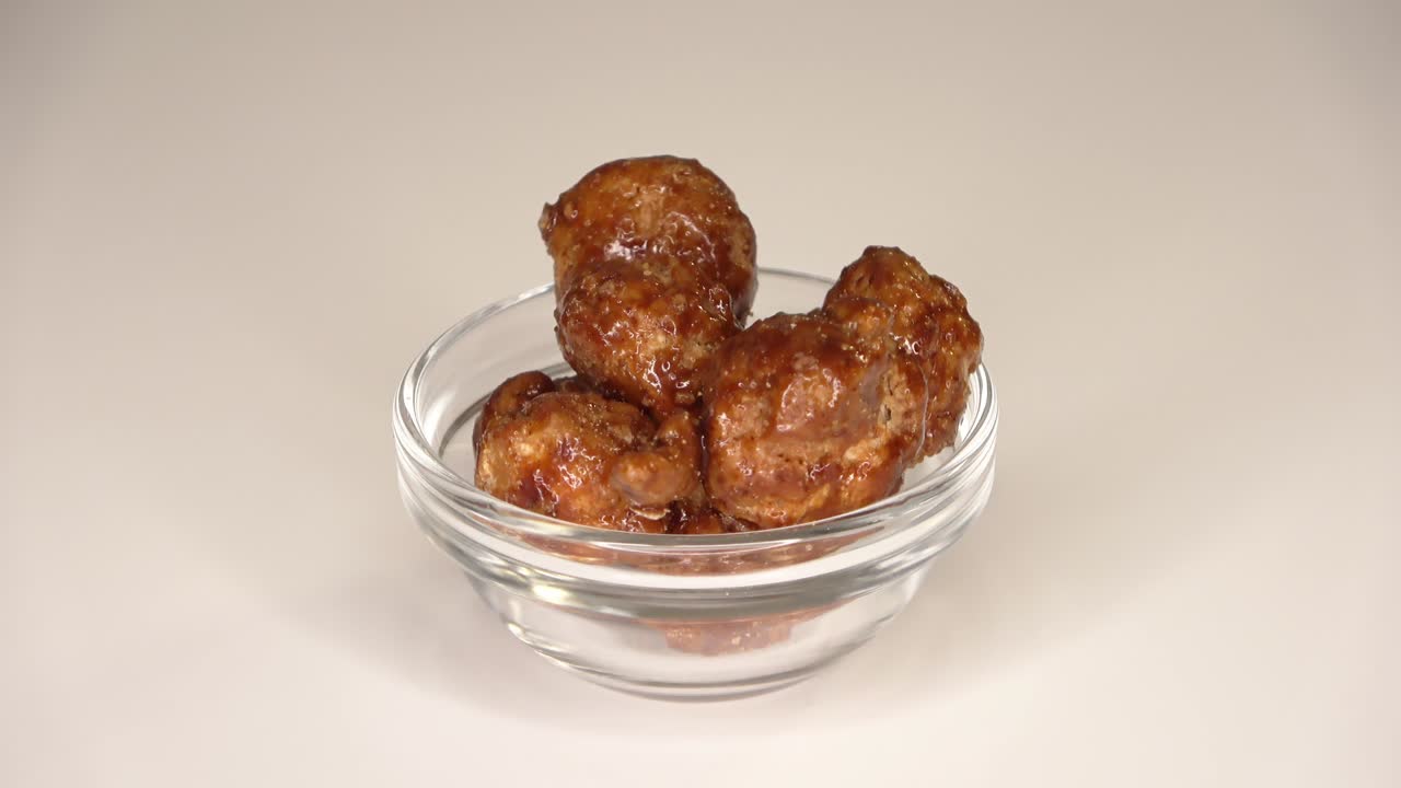 imágenes en bucle de muchas nueces de macadamia confitadas girando en un pequeño cuenco contra un fondo blanco.