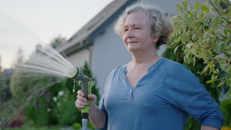 una mujer anciana riega el jardín de la casa