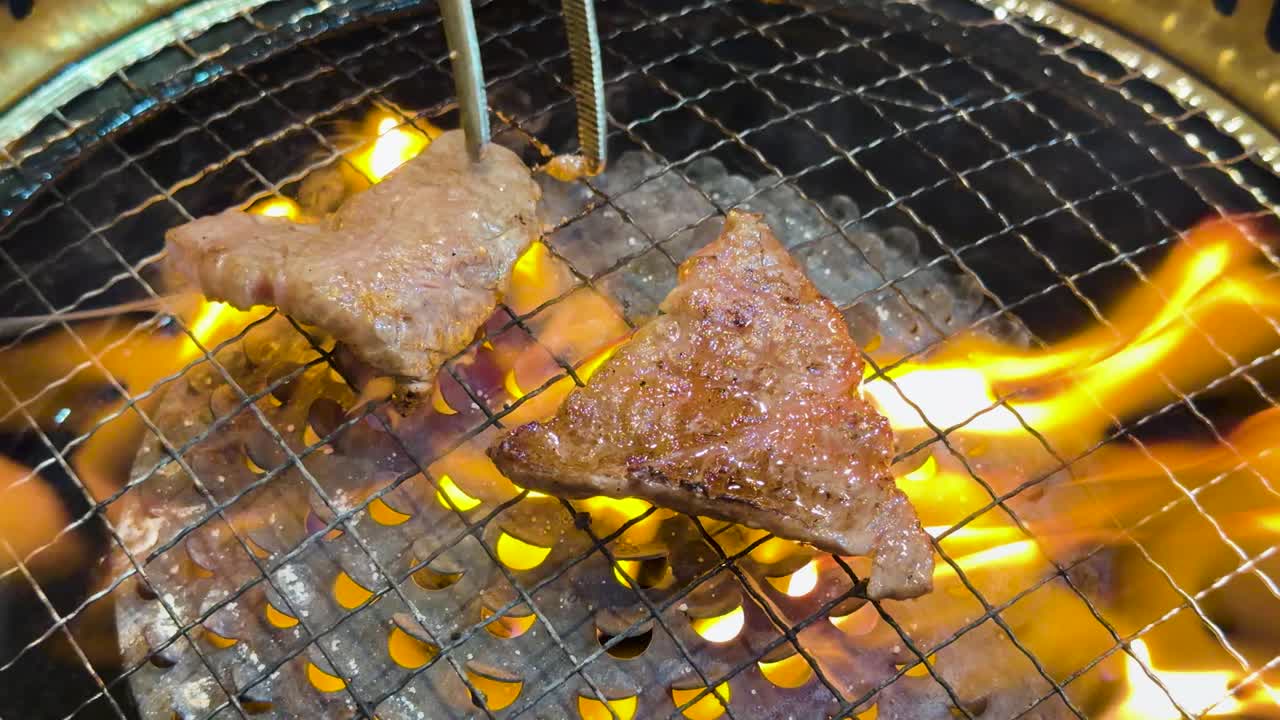 鮮やかなオレンジ色の炎を上げて熱い炭火で焼かれる霜降り牛肉のスライスのクローズアップショット。
