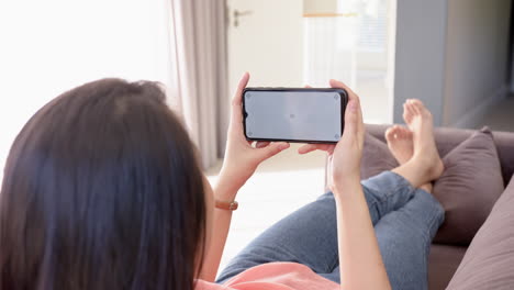 relaxing on couch, woman holding smartphone and watching video content