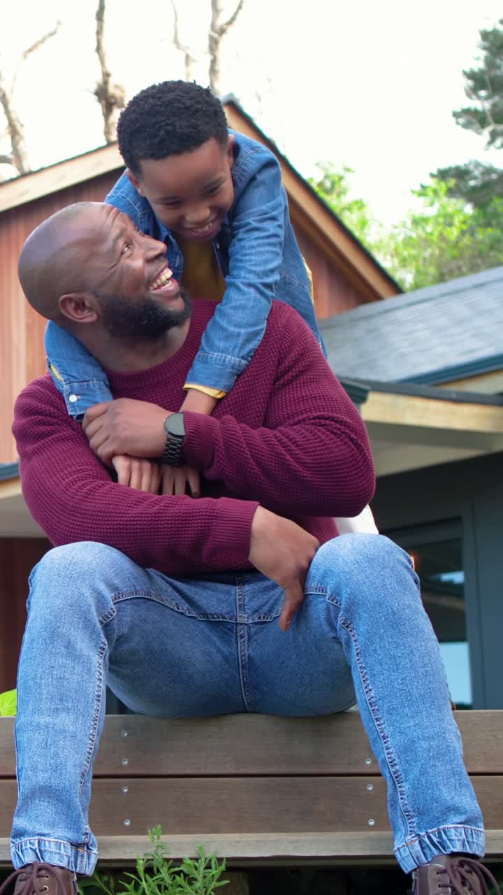 Vertical video: Climbing kid onto dad's back, dad steadying on porch, denim jacket, watch, playing