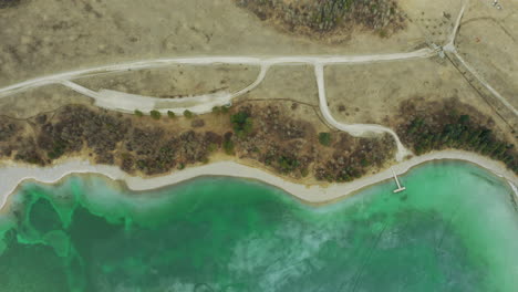 Aerial-drone-shot-of-large-bright-green-teal-lake-with-sandy-shore-and-trees-surrounding