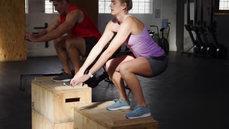 Side-view-athletic-Caucasian-man-and-woman-jumping-onto-boxes-