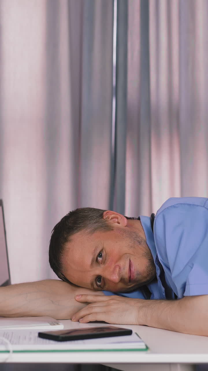 portrait of young doctor takes off his protective mask, smiles end of work shift, lies down on white table, in his office, peacefully