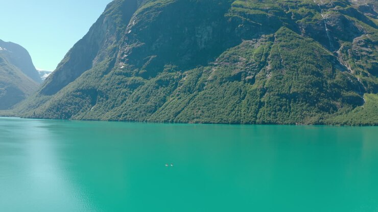 Vista lontana di barche a vela su un lago incontaminato con montagne di foreste lussureggianti vicino a Stryn, Contea di Vestland, Norvegia.