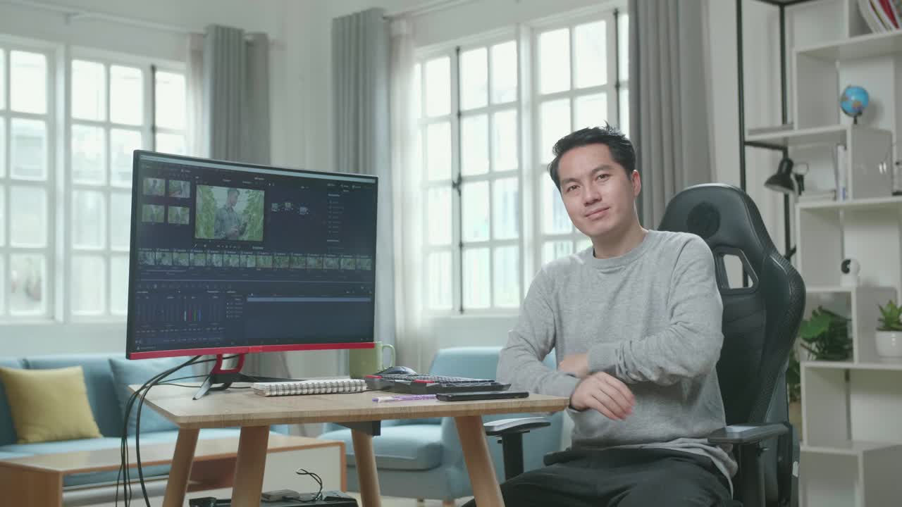Asian Video Editor Man In Long Sleeved T-Shirt And Black Pants Crossing His Arms And Smiling Due To Successful Editing Video By Desktop Computer At Home.