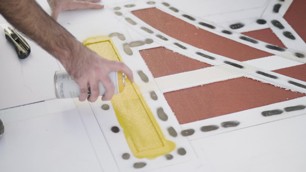 Spraying yellow paint on a stencil for creating a design or marking an area