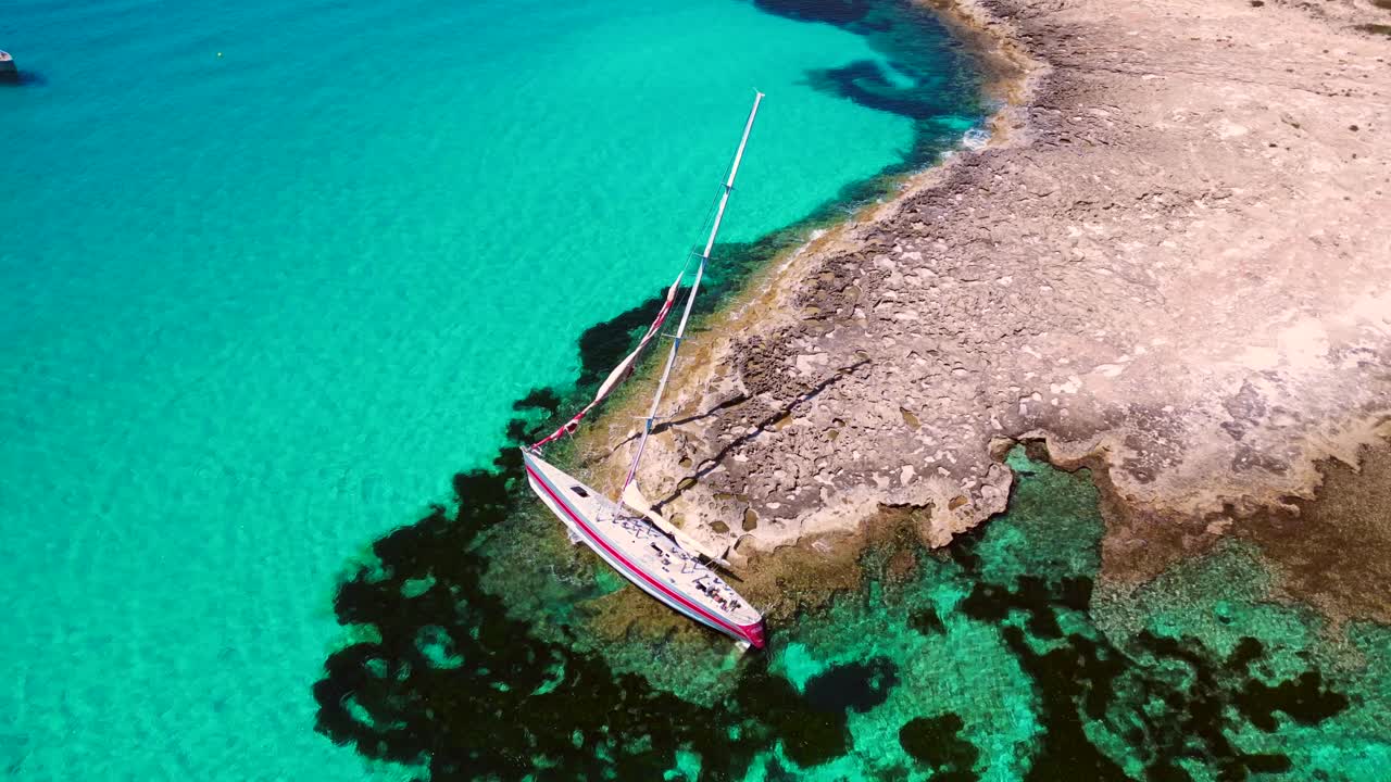 Sailboat stranded on cliff near the coast of Formentera Island, Spain, during a summer sunny day. Breathtaking aerial view flight drone shot footage from above