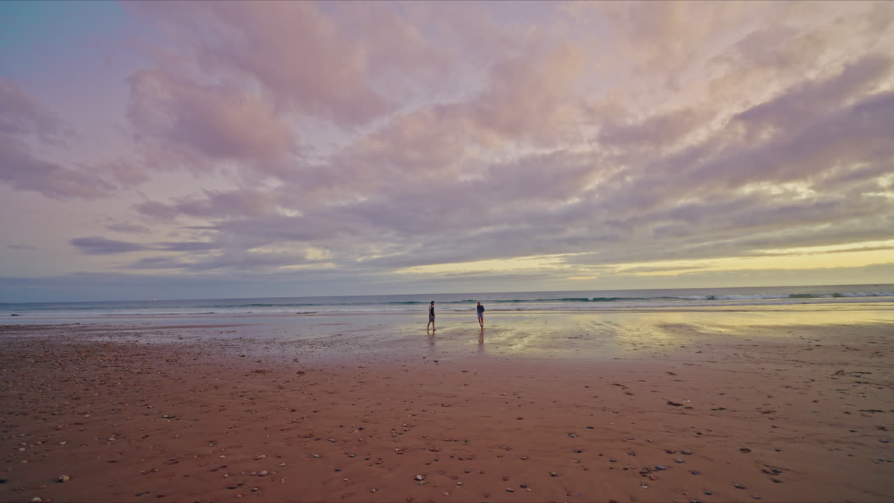 Panoramic view of two friends playing soccer on the beach of Taghazout in Morocco at sunset. Twilight coastline. Peaceful scene. Golden hour in Morocco