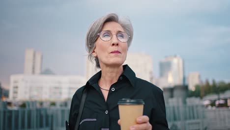 close up outdoor portrait of a business lady during lunchtime, mature woman drinks coffee and holds a folder with documents