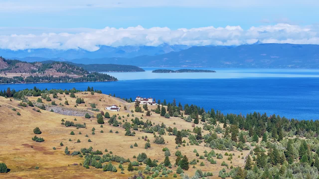 Casa sulla collina dorata con vista su un lago azzurro intenso, montagne in lontananza e un vasto orizzonte sotto la luce del giorno, Flathead Lake, Montana, USA