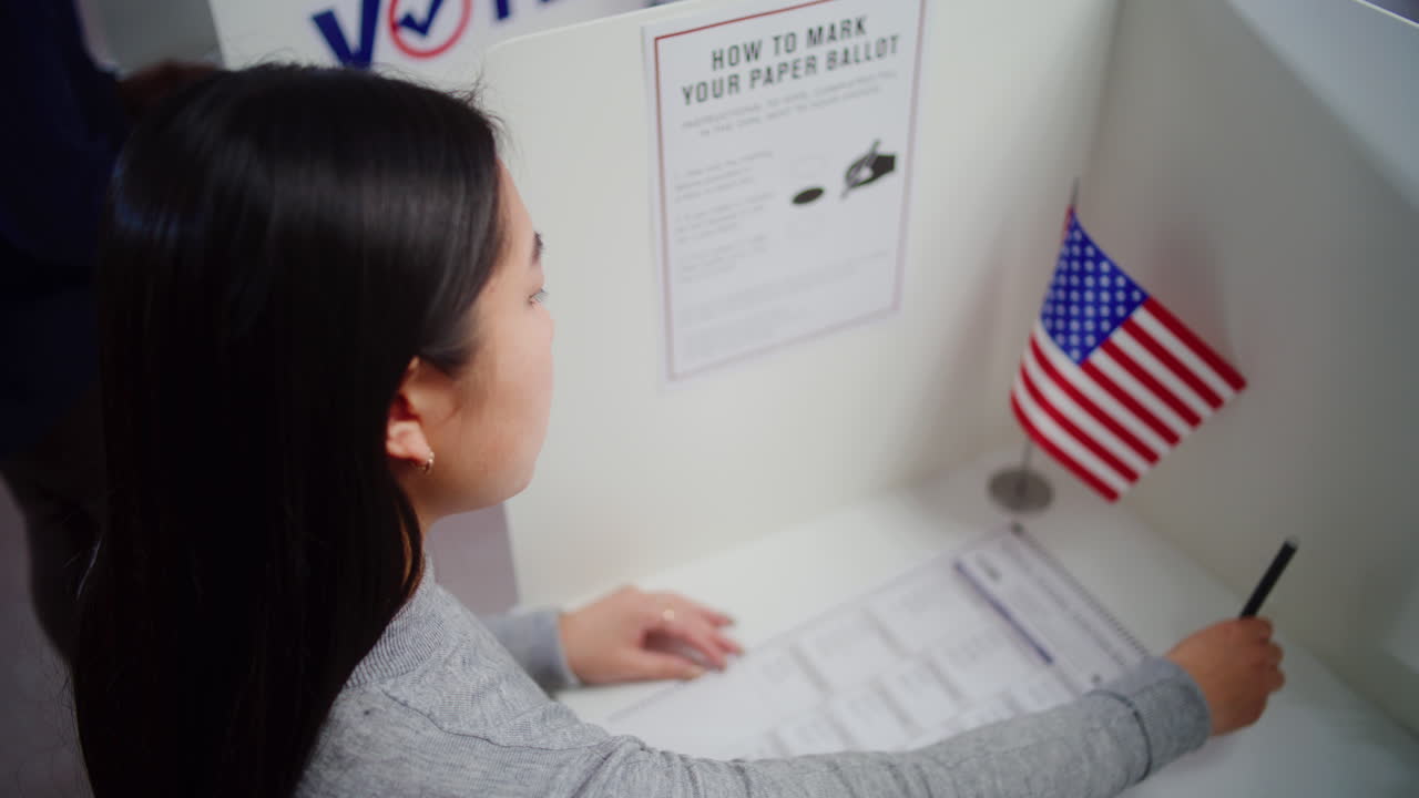 Asian Woman Comes to Voting Booth and Fills out Paper Bulletin Asian Woman Comes to Voting Booth at Polling Station Makes Choice and Fills out Paper Bulletin us Citizen during National Election Day in the United States of America Civic Duty and Patriotism