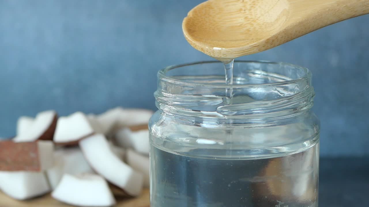 vertiendo aceite de coco de una cuchara de madera en un frasco de vidrio
