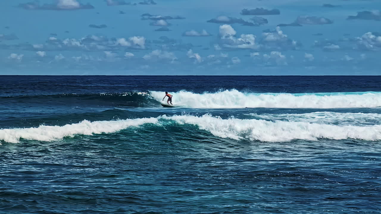 Profile view of a lone surfer rideing turquoise water of ocean under partially cloudy sky in Nyang Nyang Beach of Bali, Indonesia.
