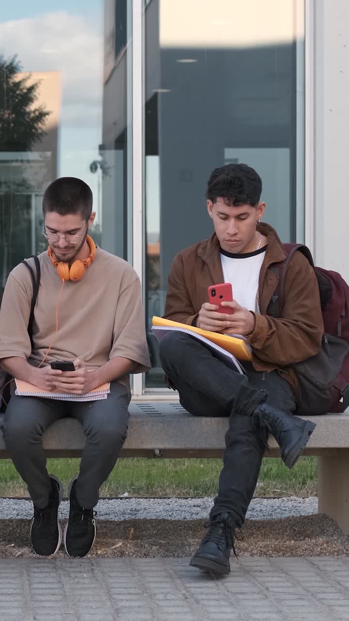 Couple of friends sitting on a bench using mobiles