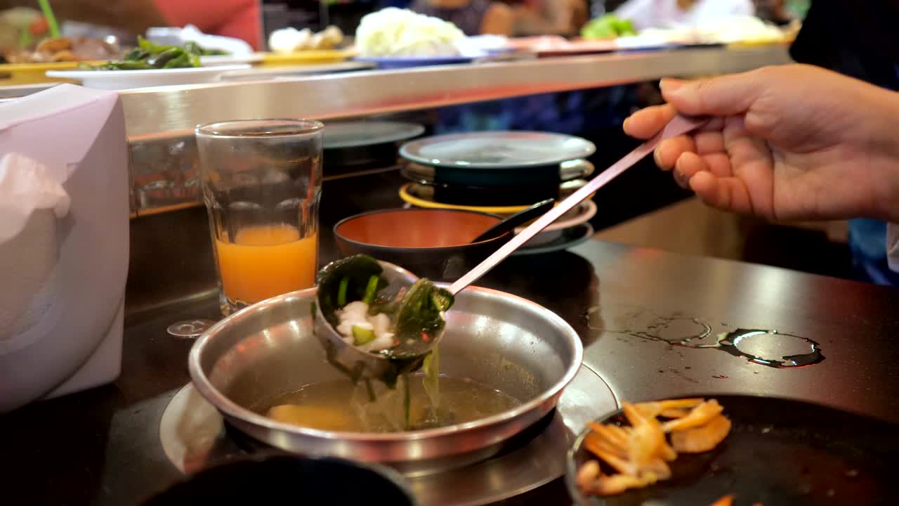 여자 는 접시 와 함께 움직이는 컨베이어 의 배경 에 대 한 뷔페 에서 해산물 수프 를 준비 하고 있다