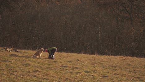 Woman-digging-in-backpack-while-golden-retriever-pet-waits-patiently-watching-her