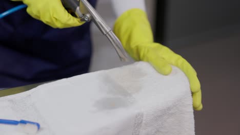 hands in gloves drying spot on towel with stain removed at laundry shop