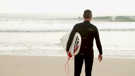 man with surfboard walking to ocean