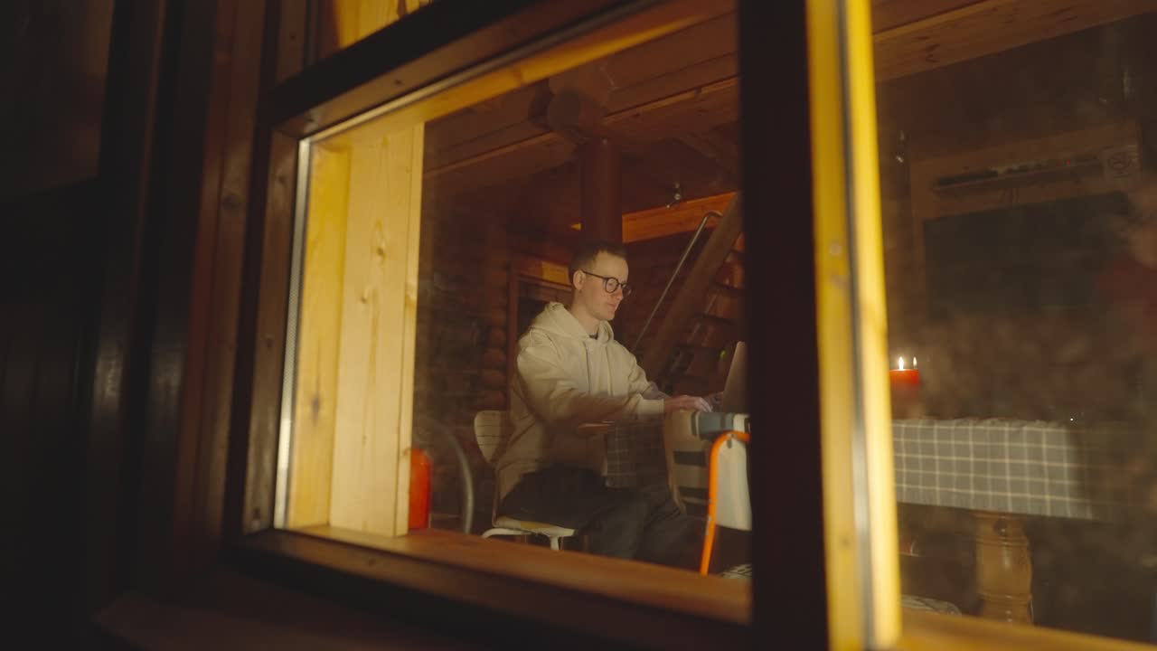 el hombre se sienta cerca de la computadora portátil en una acogedora cabaña de madera